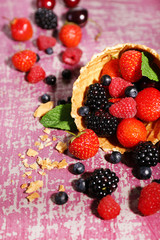 Different ripe berries in sugar cone, on purple background