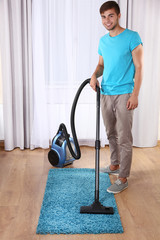 Fototapeta premium Young man doing vacuum cleaning in room