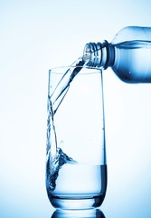 Pouring water into glass  from bottle on blue background