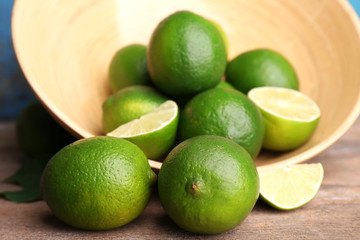 Fresh juicy limes in bowl on old wooden table
