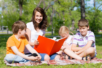Fototapeta premium teacher reads a book to children in a summer park