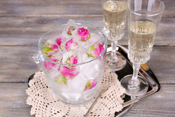 Ice cubes with rose flowers in glass bucket and two glasses