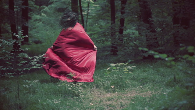 Woman in red cape running away in forest