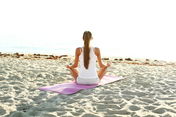 Fototapeta na wymiar young woman doing yoga on the beach at sunrise.