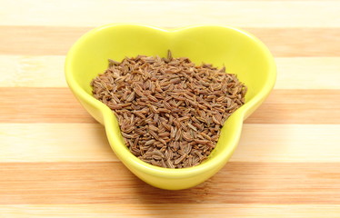 Cumin seeds in yellow bowl on wooden cutting board