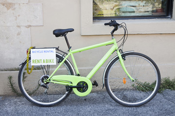 Fototapeta na wymiar Green bicycle for rent against the wall