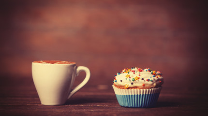 Cup of coffee and cupcake on wooden table.