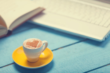 Cup of coffe with laptop and book on blue wooden table.