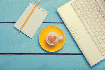 cup of coffee and laptop with note on blue wooden table.