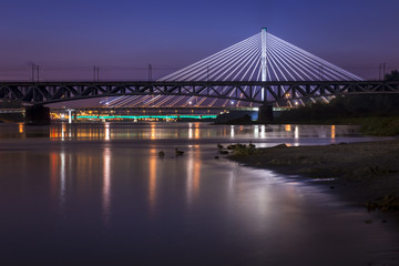 Backlit bridge at night and reflected in the water