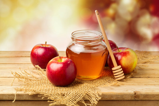 Apples with honey jar on wooden table over bokeh background