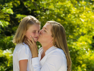 Fototapeta premium Mother kissing her young daughter on side of face