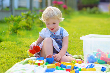 Happy toddler girl playing with colorful plastic toys outdoors