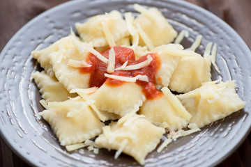 Cheese ravioli with tomato sauce and parmesan on a glass plate