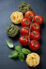 Red tomatoes on a branch, colored tagliatelle and green basil