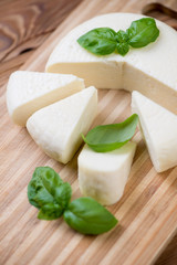 Sliced round cheese and green basil, close-up, vertical shot