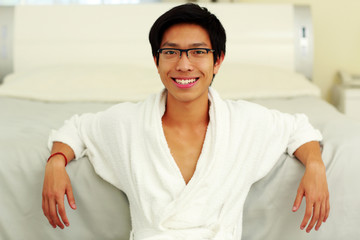 Happy man in bathrobe leaning on the bed in bedroom