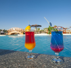 Two cocktail drinks by a tropical pool