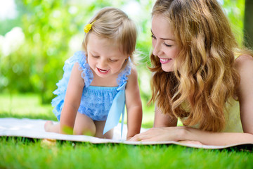 Young mother with little daughter reading book in park