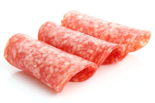 Thin slices of salami rolled into shape on white background.
