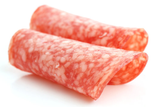 Thin slices of salami rolled into shape on white background.