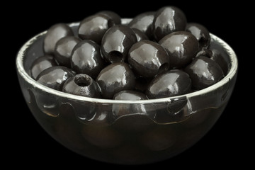 Glass bowl of stoned black olives on black background.