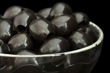 Glass bowl of stoned black olives on black background.