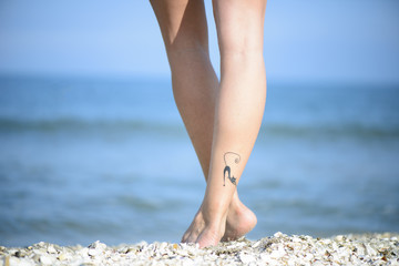 Closeup detail of female feet with cat tattoo on a beach