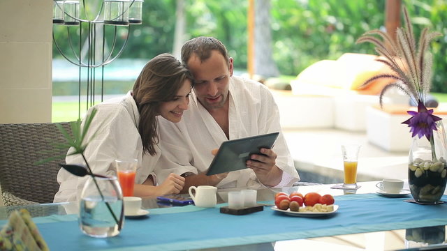 Couple chatting over tablet computer by table in luxury villa
