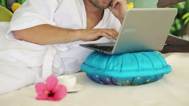Man with laptop having break for coffee and relax on gazebo bed