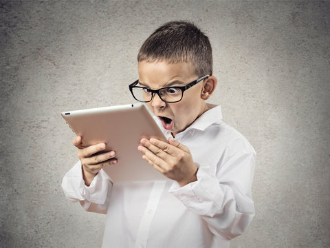 Shocked, frustrated boy using pad computer, grey background