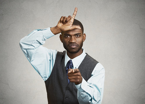 Bully boss executive man giving loser sign, grey wall background