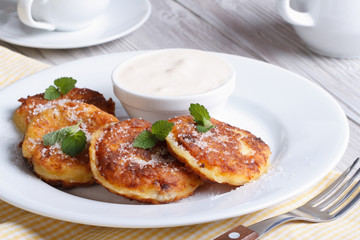 Portion cheese pancakes on a white plate with sour cream