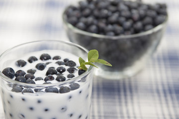 Blueberries with yogurt in a glass and blueberries in a vase.