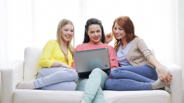three smiling teenage girls with laptop at home