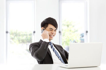 young business man talking happily by smart phone in office