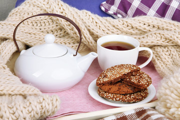 Cup and teapot with cookies on tray and scarf on bed close up