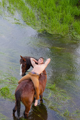 man lies on grain of the horse standing in water, and looks up