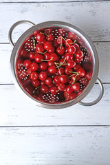 Sweet cherries in colander on color wooden background