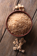 Brown sugar cubes and crystal sugar in bowl on wooden
