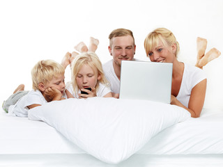 Smiling family with laptop stay in bed