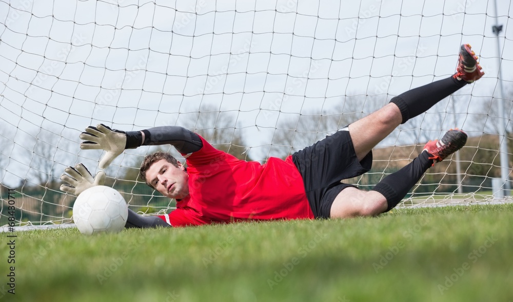Poster goalkeeper in red saving a goal during a game