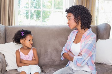 Pretty mother sitting on couch with petulant daughter