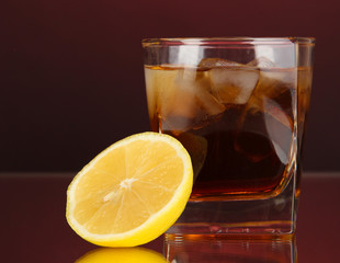 Glass of whiskey with ice and lemon on red background