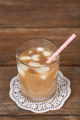 Iced coffee with milky ice cubes in glass on wooden background