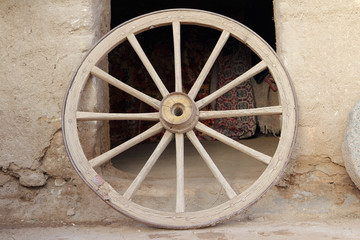 An old wooden wagon wheel leaning up against soil wall