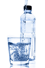 Water pouring into glass with bottle isolated on white.