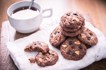 Chocolate chip cookies on napkin and hot tea on wooden table.