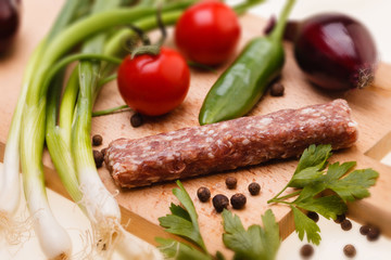 raw kebapcheta with vegetables on wooden board