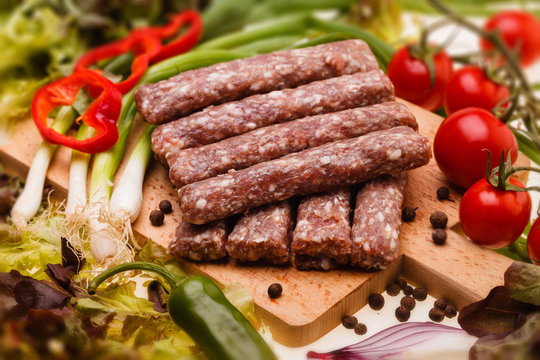 raw kebapcheta with vegetables on wooden board